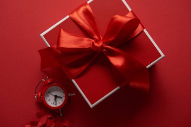 top view of red present with silk ribbon, clock and paper cut hearts on red background clipart