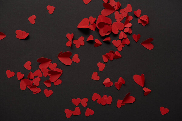 top view of red small paper cut hearts on black background