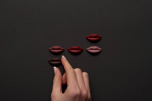 cropped view of female hand and multicolored chocolate lips on black background 