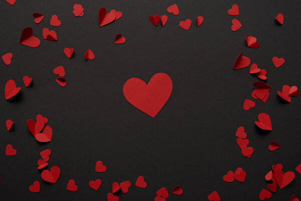 top view of big and small paper cut red hearts on black background