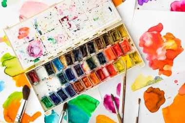 top view of paints and paintbrushes on papers with abstract watercolor spills clipart