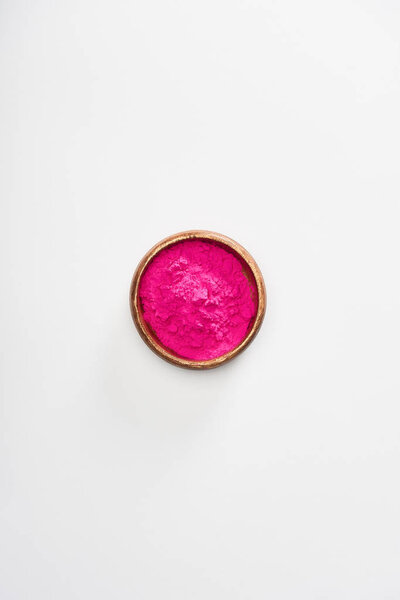 top view of wooden bowl with pink holi powder on white background