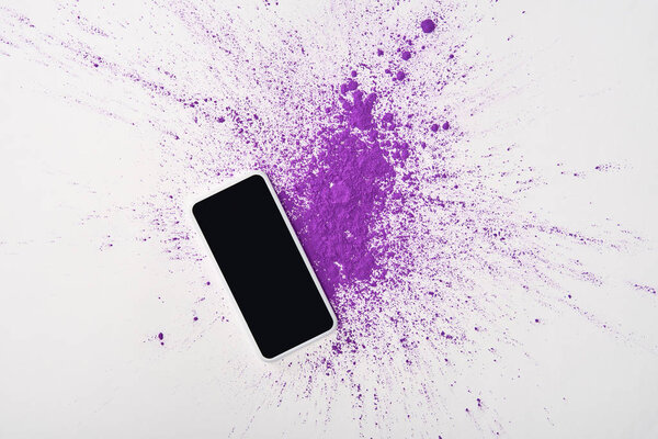 top view of smartphone with blank screen and explosion of purple holi powder on white background