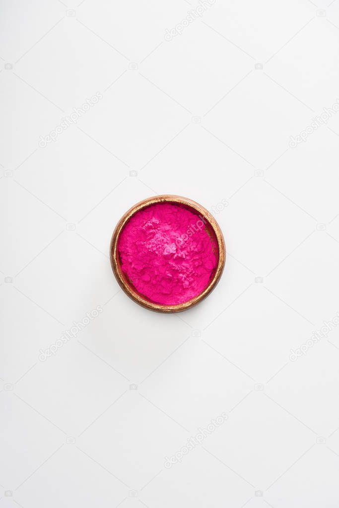 top view of wooden bowl with pink holi powder on white background