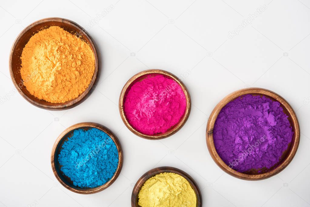 top view of wooden bowls with pink, blue, yellow, purple and orange holi powder on white background