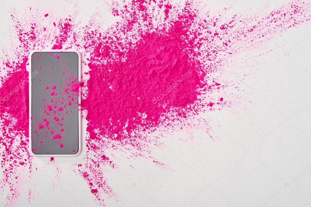 top view of smartphone and explosion of pink holi powder on white background