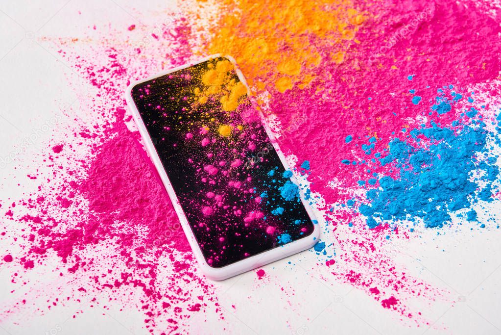 top view of smartphone and explosion of multicolored holi powder on white background