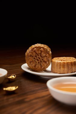 selective focus of mooncakes with tea cup and gold ingots isolated on black clipart