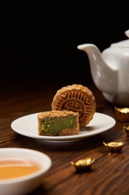 seçici odak geleneksel Çin mooncakes, çay potu ve ahşap masa üstünde siyah izole üzerinde altın İngotlar