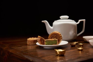 geleneksel lezzetli Çin mooncakes, çay potu ve ahşap masa üstünde siyah izole üzerinde altın İngotlar