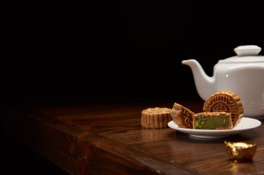 Geleneksel Çin mooncakes, çay potu ve siyah kopya alanı ile izole ahşap masa üzerinde altın külçe
