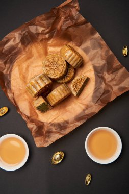 top view of chinese mooncakes with tea cups isolated on black clipart