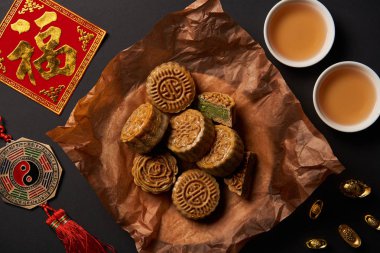 top view of traditional mooncakes with chinese talismans and tea isolated on black clipart