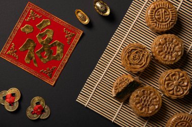 top view of traditional mooncakes with chinese talismans and bamboo table mat isolated on black clipart