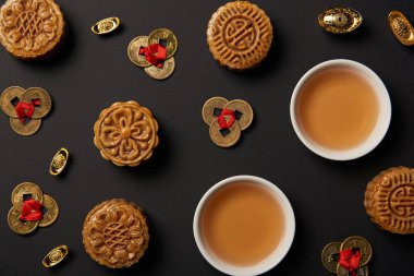 top view of traditional mooncakes, tea cups and feng shui coins isolated on black clipart