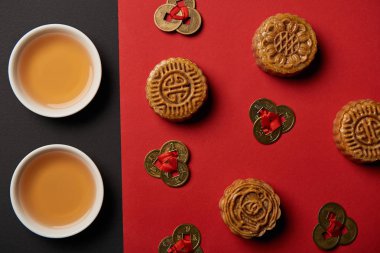 top view of mooncakes, feng shui coins and cups with tea on red and black background clipart