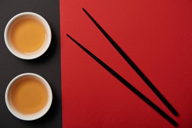 top view of tea cups and chopsticks on red and black background  clipart