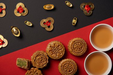 top view of mooncakes, feng shui coins and cups with tea on red and black background clipart