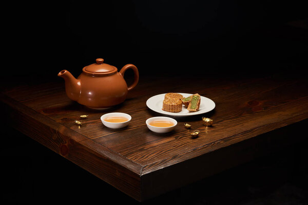 tea pot, mooncakes and cups on wooden table isolated on black