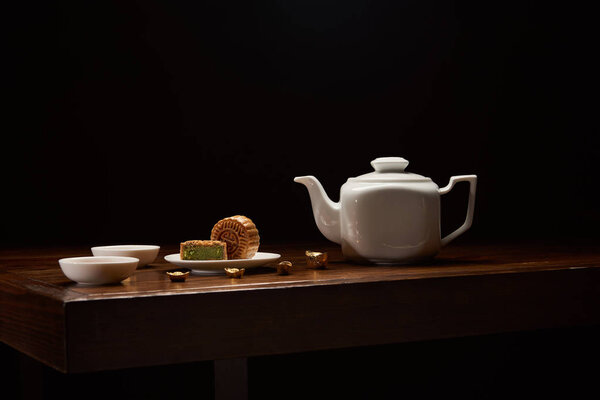 traditional chinese mooncakes, tea pot and gold ingots on wooden table isolated on black with copy space