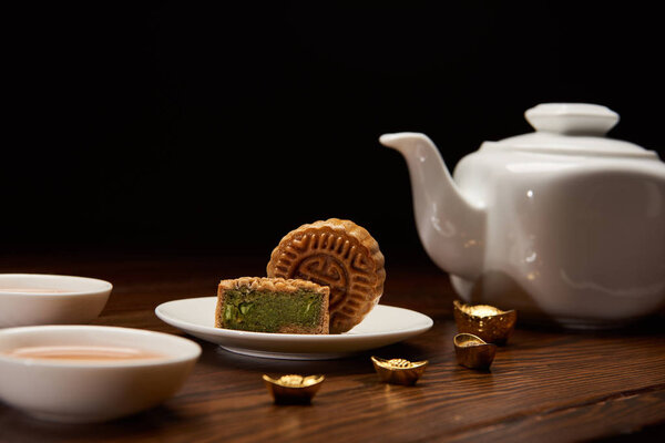 traditional delicious chinese mooncakes, tea pot and gold ingots on wooden table isolated on black