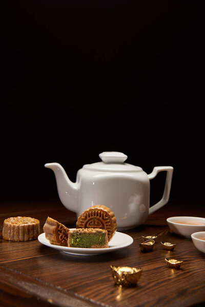 traditional chinese mooncakes, tea pot and gold ingots on wooden table isolated on black