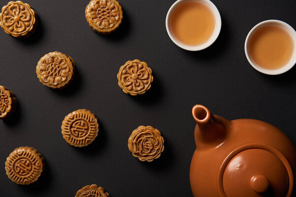 top view of mooncakes, tea pot and cups isolated on black