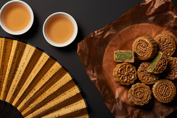 top view of traditional chinese mooncakes with tea and hand fan isolated on black