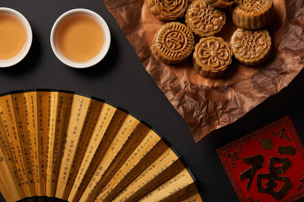 top view of traditional chinese mooncakes with tea and hand fan isolated on black