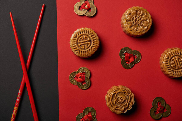 top view of mooncakes, feng shui coins and chopsticks on red and black background