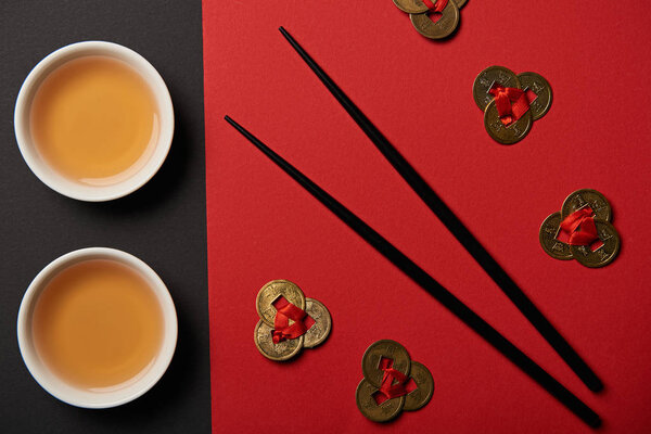 top view of tea cups, feng shui coins and chopsticks on red and black background 