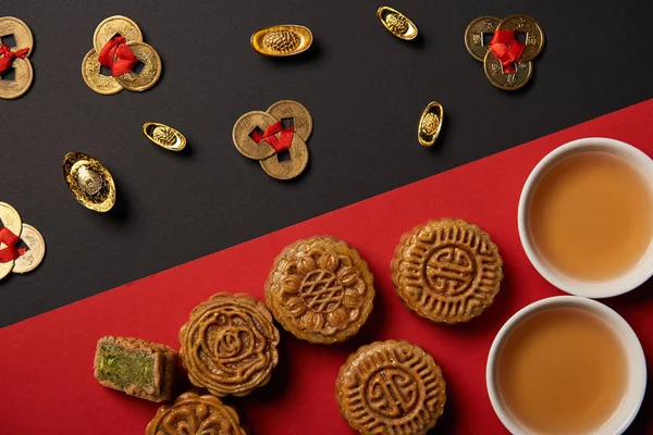 kırmızı ve siyah arka plan üzerinde mooncakes, feng shui sikke ve bardak çay ile üstten görünüm
