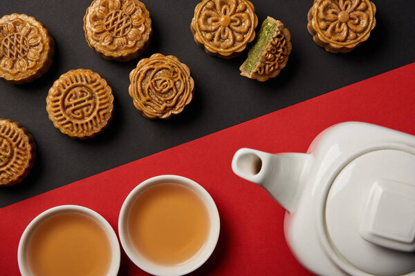 top view of mooncakes, tea pot and cups on red and black background 