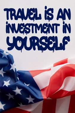 top view of united states of america flag and travel is an investment in yourself quote on white surface 