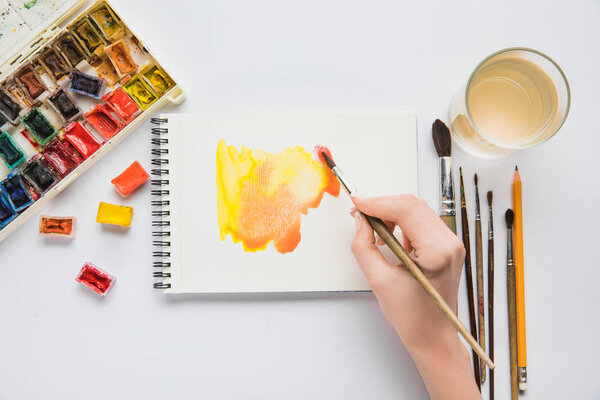 top view of female hands drawing in album with watercolor paints and paintbrush