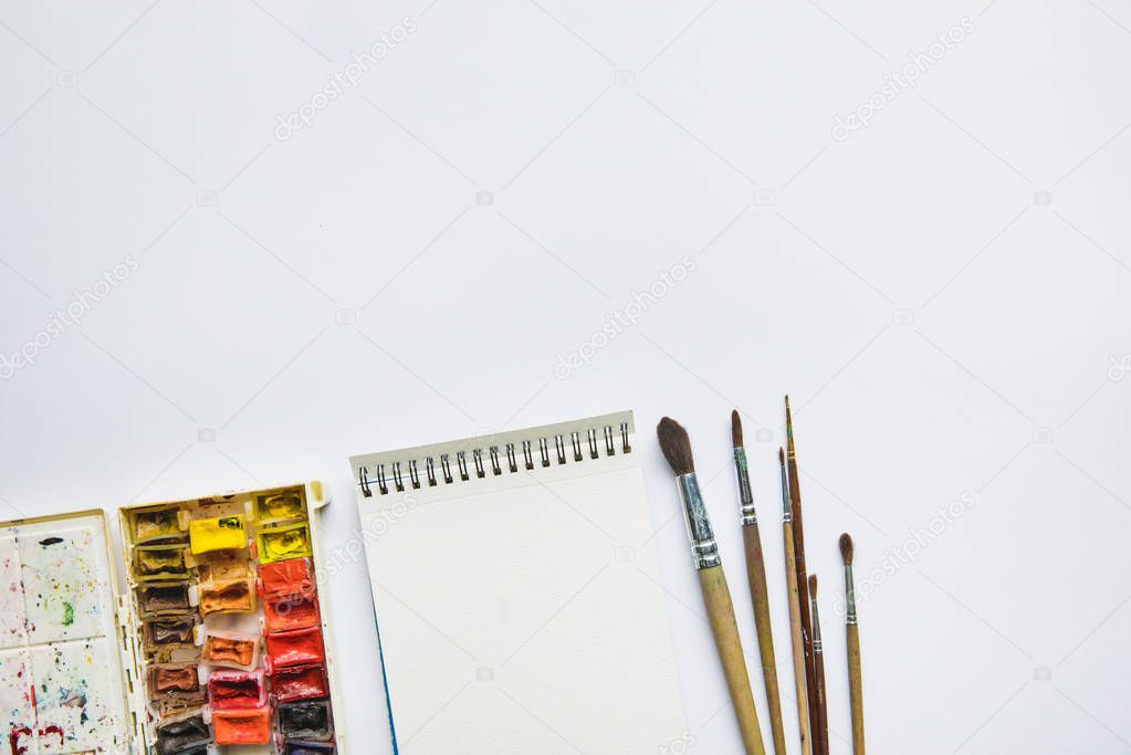top view of white background with album for drawing, multicolored paints and paintbrushes