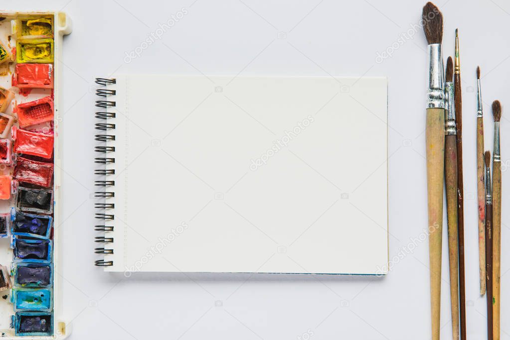 top view of white background with album for drawing, multicolored paints and paintbrushes 