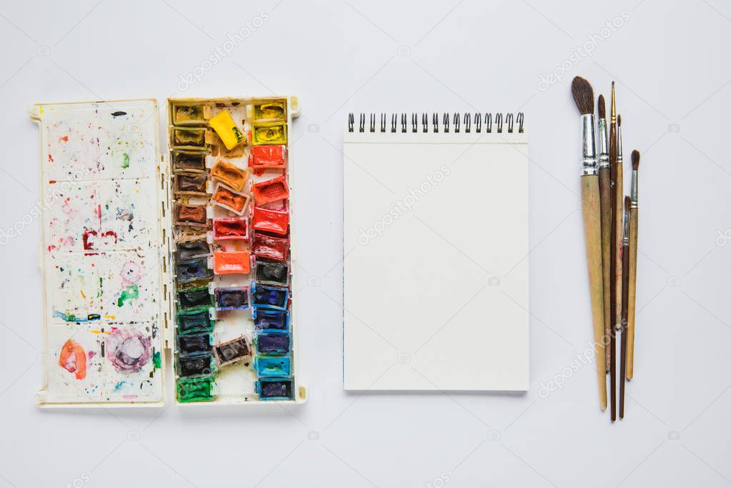 top view of album with watercolor paints and paintbrushes on white background