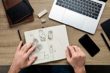 top view of mans hands laying on wooden table along album with sketches, laptop and a smartphone clipart
