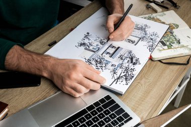 selective focus of mans hands drawing in album on wooden table next to  utensils clipart