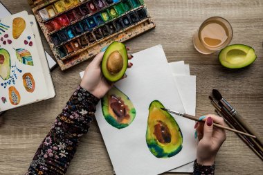 Kadın el ahşap masa üzerinde avokado suluboya boya ve boya fırçası ile çizim üstten görünüm