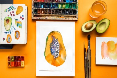 sarı arka plan üzerinde renkli boyalar ve boya fırçaları yanındaki papaya çizimlerinin üstten görünüm 