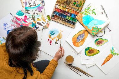 renkli çizimler ve çizim gereçleri çevrili iken suluboya boya ile resim kadının üstten görünüm