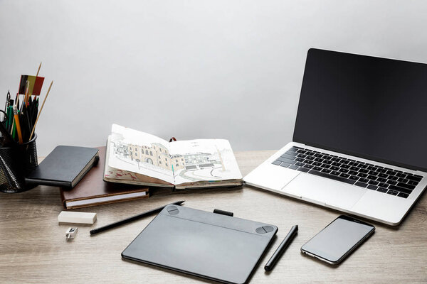selective focus of wooden table with laptop, smartphone and drawing utensils