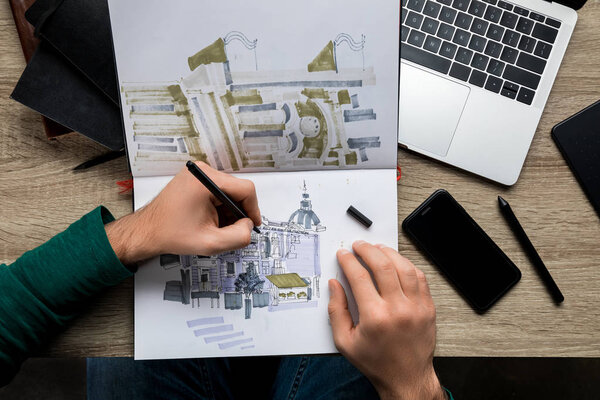 верхний вид мужчин руки рисования в альбом на деревянном столе рядом с ноутбуком и смартфоном
