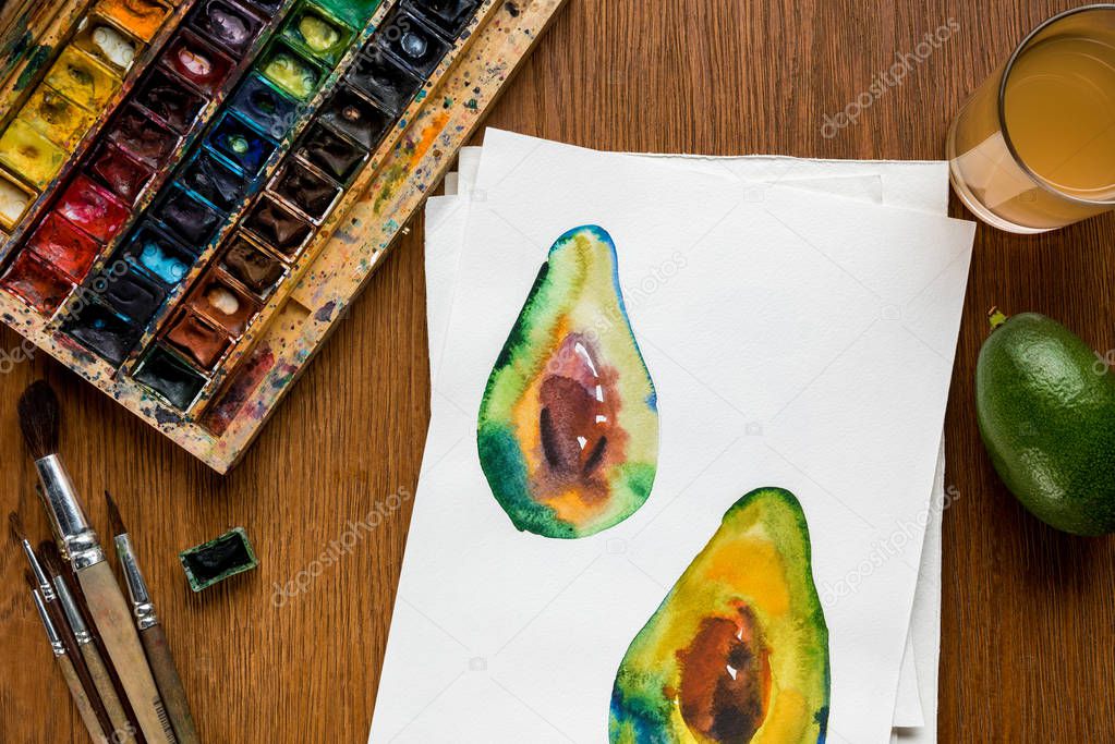 top view of colored paints, paintbrushes and drawing with avocado on wooden background