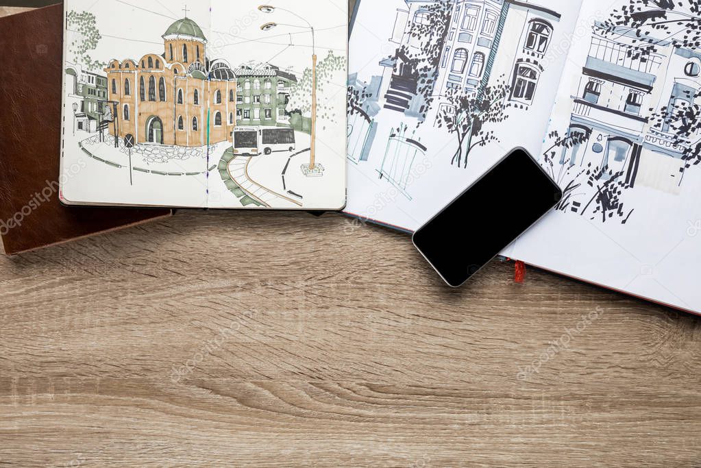 top view of drawings in albums and smartphone on wooden background