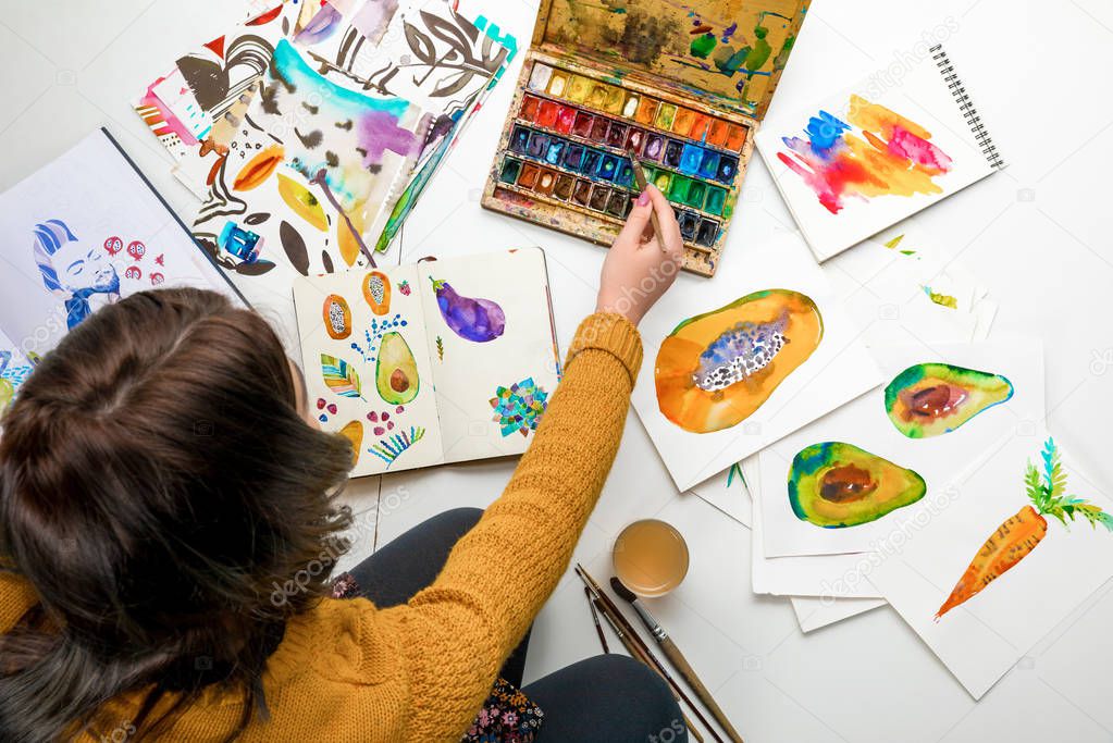 top view of woman women mixing watercolor paints while surrounded by color drawings