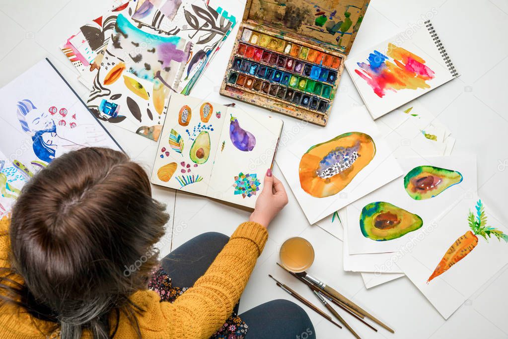 top view of sitting woman surrounded by color drawings and drawing utensils