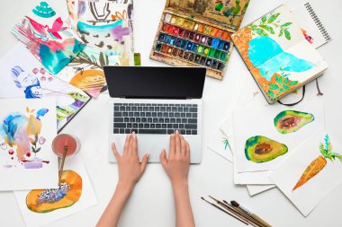 top view of female hands on laptop while surrounded by watercolor drawings clipart